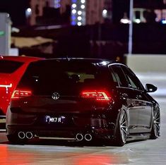 two cars parked next to each other in a parking lot at night with lights on