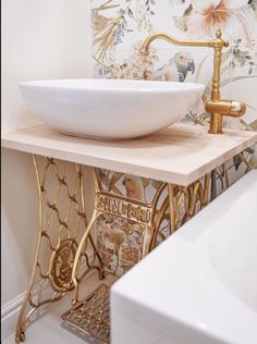 a bathroom sink with a gold faucet next to a white bathtub and wallpaper