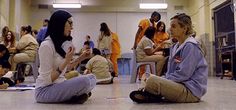 two women sitting on the floor talking to each other while others sit and stand around