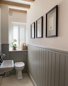 a white toilet sitting next to a sink in a bathroom under three framed pictures on the wall