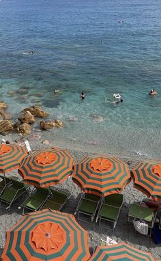 many orange and green umbrellas are on the beach near some people swimming in the water