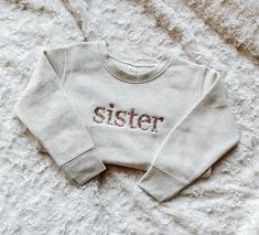 This sweet sister sweatshirt is embroidered with beautiful floral details.  This shirt is perfect for any little girl whether they are already a sister or are about to become one. This cozy sibling sweatshirt can be paired with one of our baby announcement signs to provide the perfect announcement that you are adding to your family! Important Details: For sizes 2T - 7:  Sweatshirt is 60/40 cotton/polyester fleece For sizes 6-12 months - 18-24 months:  Pullover is 100% cotton.  This is a soft lig Cute Embroidered Relaxed Fit Tops, Cute Embroidered Tops With Relaxed Fit, Long Sleeve Cotton Tops With Machine Embroidery, Cotton Long Sleeve Tops With Machine Embroidery, Cute Tops With Embroidered Text For Fall, Cute Embroidered Text Tops For Fall, Cotton Long Sleeve Tops With Letter Embroidery, Cute Floral Embroidered Long Sleeve Tops, Big Sister Gifts