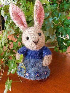 a knitted rabbit sitting on top of a wooden table next to a potted plant