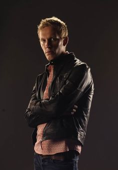 a man in a leather jacket is standing with his arms crossed