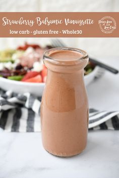 a close up of a jar of food on a table with a salad in the background