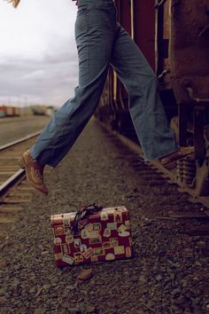 a woman is walking on the train tracks with her suitcase and shoes in front of her