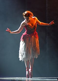 a woman in a red and white dress on stage with her arms out to the side