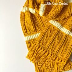 a yellow and white knitted scarf with fringes on the ends, sitting on top of a table