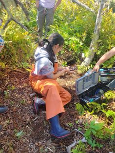 two people standing in the woods looking at something on a piece of equipment that they are holding