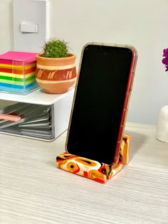 a cell phone on a stand next to a potted plant and other office supplies