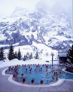 people in a swimming pool surrounded by snow covered mountains