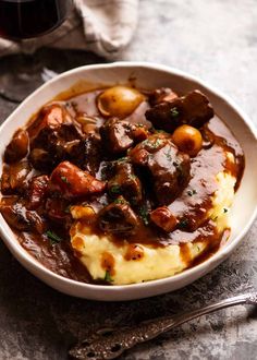 a bowl filled with meat and potatoes covered in gravy next to a glass of wine