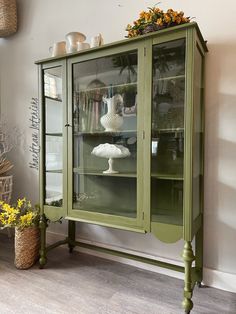 a green china cabinet with glass doors and flowers in the vases next to it