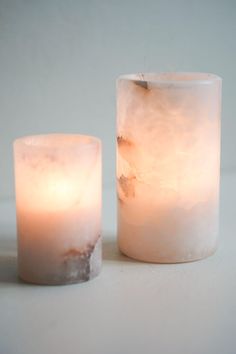 two lit candles sitting next to each other on a white counter top, one is frosted with ice