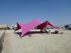 a large pink tent sitting on top of a sandy beach next to a fence and parked cars