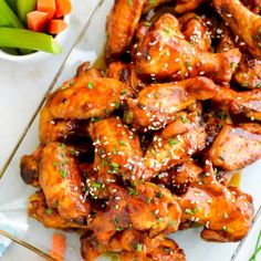 chicken wings with sesame seeds and carrots on a plate next to a bowl of celery