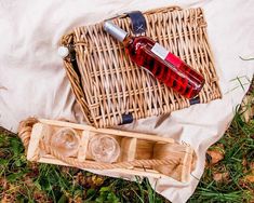 a bottle of wine and two glasses sitting on top of a wicker picnic basket