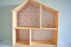 a wooden doll house with flowers on the walls and floor, in front of a wallpapered background