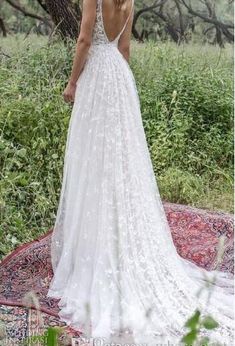 a woman in a wedding dress standing on a rug looking at the trees and grass