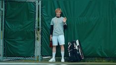 a young man standing next to a tennis racket and bag on a tennis court