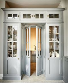 an open door leading into a kitchen with white cabinets and glass doors on both sides