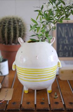 a white pig planter sitting on top of a wooden table next to a potted plant