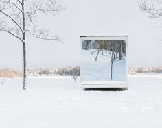 a white box sitting in the middle of a snow covered field next to two trees