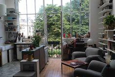 a living room filled with furniture next to a window covered in lots of books and plants