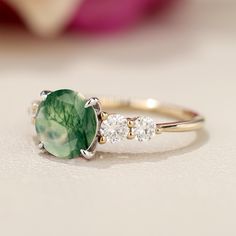 a close up of a ring with a green stone and three diamonds on the side