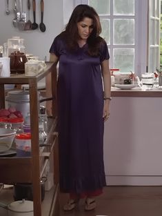 a woman in a purple dress standing next to a counter full of dishes and utensils