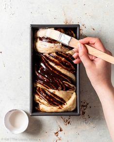 a person is spreading chocolate on top of banana bread in a pan with a wooden spatula