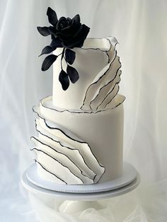 a three tiered white cake with black flowers on top