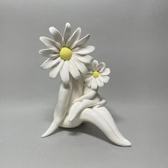 a white ceramic flower vase sitting on top of a planter with two daisies in it