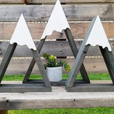 three wooden triangle shaped sculptures sitting on top of a wood bench in front of a fence