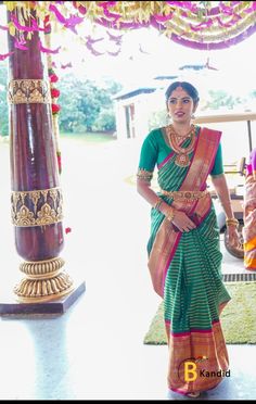 a woman in a green and red sari standing next to a pillar with flowers on it