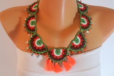 a woman wearing a green and red crochet necklace with orange tassels