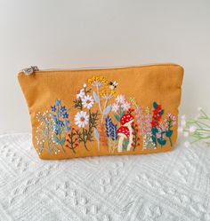 a small yellow pouch with flowers and mushrooms on it, sitting on a white surface