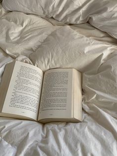 an open book laying on top of a white comforter covered in sheets and pillows