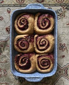 a blue dish filled with cinnamon rolls on top of a rug