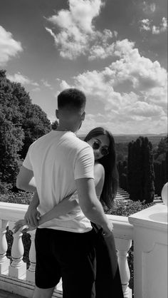 a man and woman standing next to each other on a balcony looking at the sky