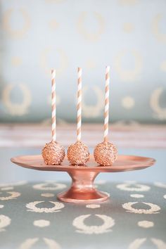 three cake pops sitting on top of a pink plate with two white and gold striped candles