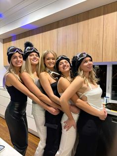 four beautiful women in black and white outfits posing for a photo with one woman holding her arms around the other