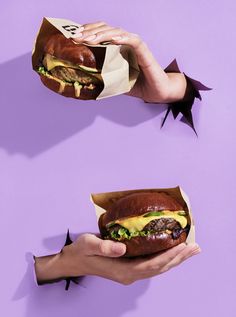 two hands holding sandwiches on top of each other in front of a purple background with black spots