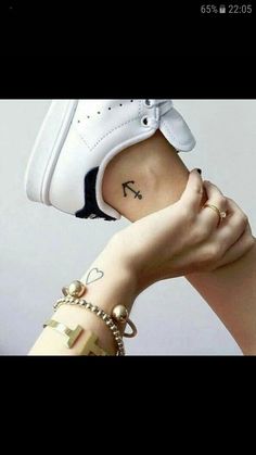 a woman's hand with a tattoo on her left arm holding up a white shoe