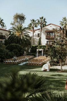 an outdoor ceremony setup with chairs set up in the grass and palm trees surrounding it