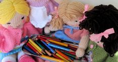 several knitted dolls with colored pencils in front of them and a tin of crayons