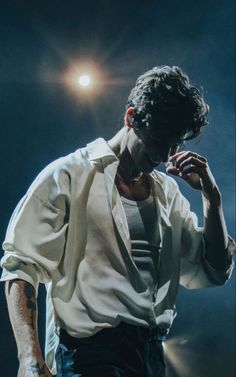 a man in white shirt and black pants holding his hand to his face while standing on stage