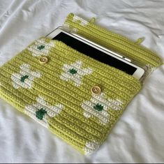 a green purse with white flowers on it sitting on top of a bed next to a cell phone