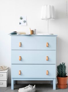 a blue dresser sitting next to a potted plant on top of a white floor