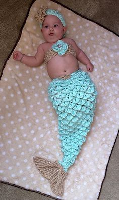 a baby laying on top of a blanket wearing a blue and white crochet mermaid tail